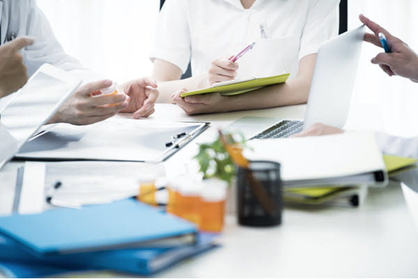 Three healthcare workers sitting around a table with binders and medicine bottles.