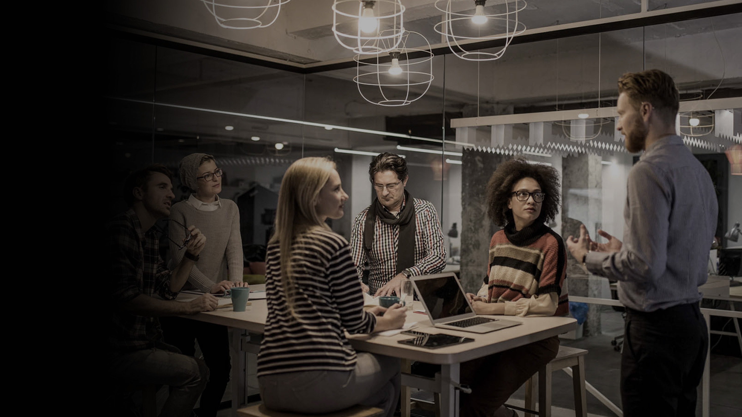 A group of teammates listening to their coworker presenting something.