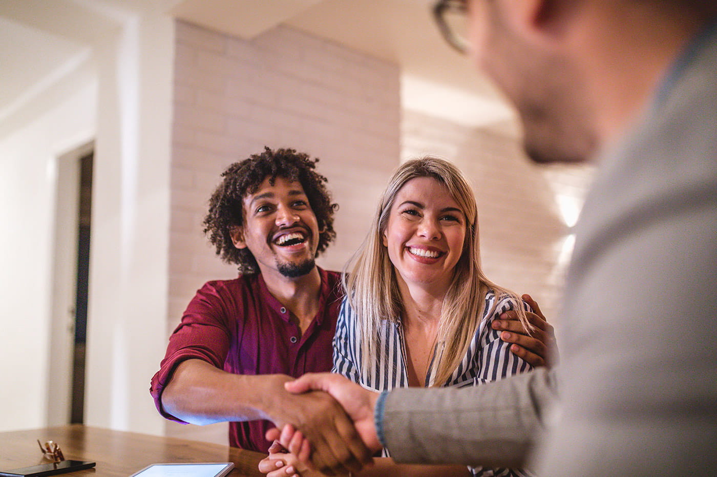 Multiracial couple shaking hands and smiling with business person.