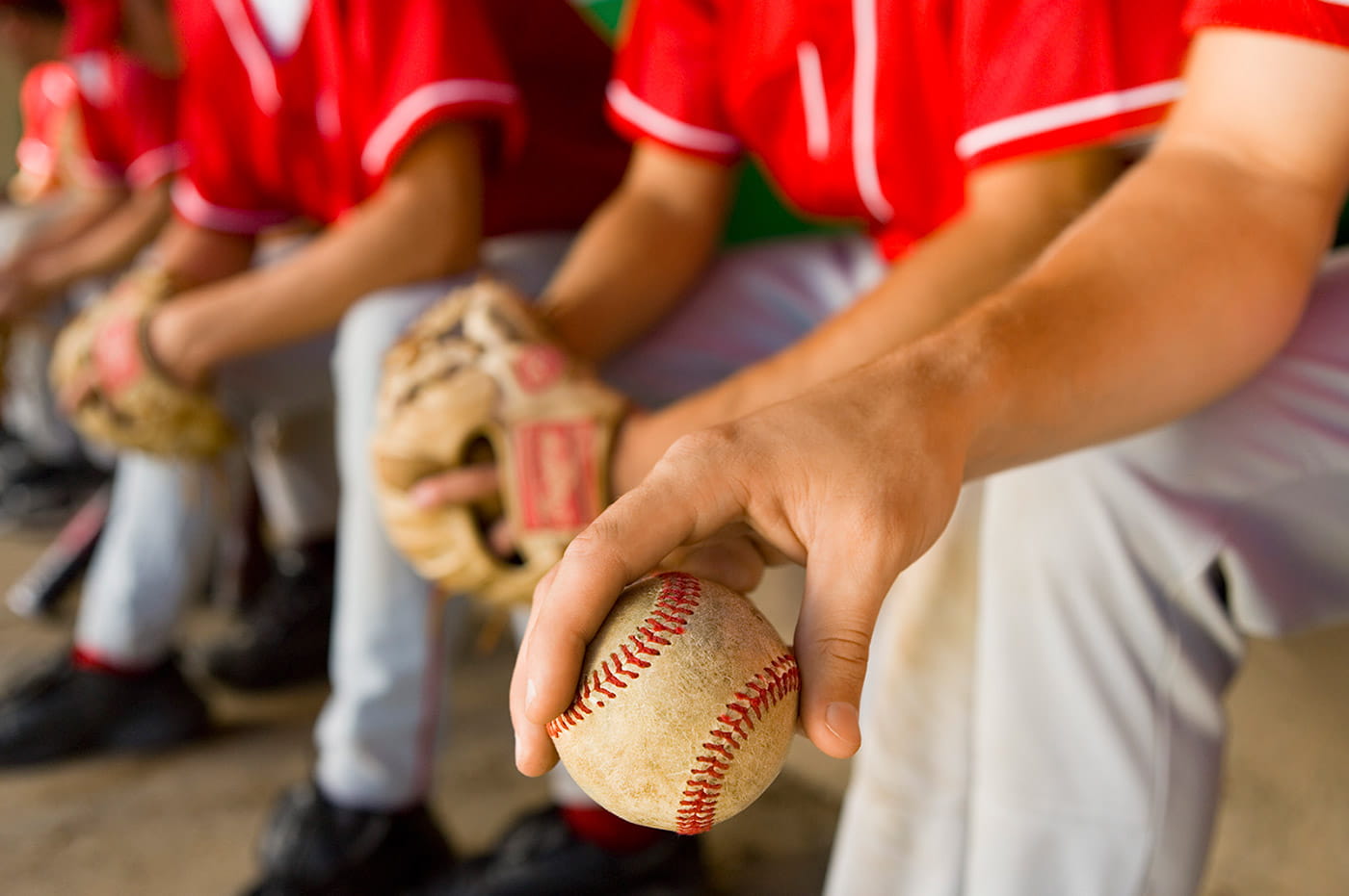 Baseball team sitting in the dugout with baseball gloves and ball.