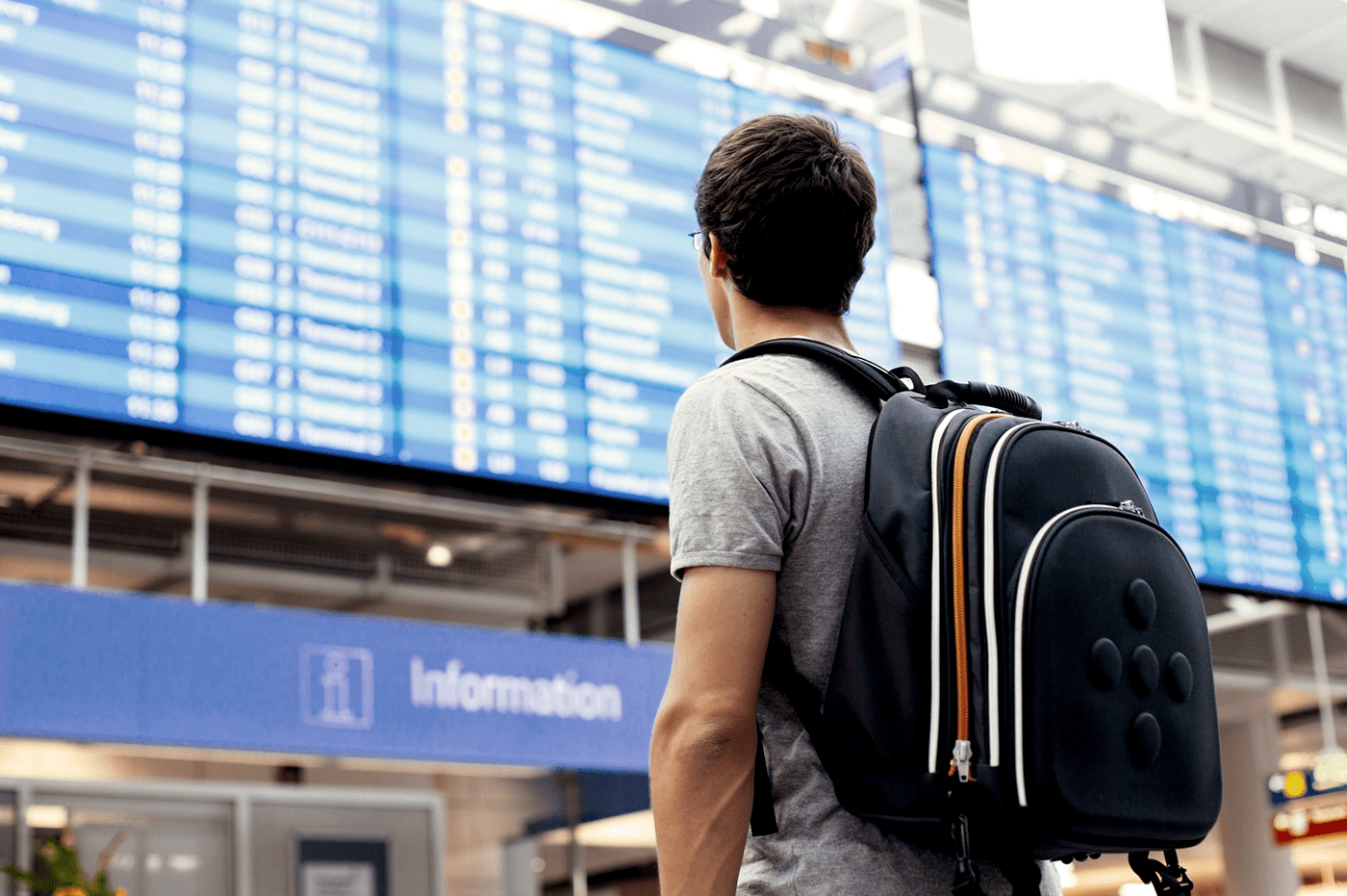 Man wearing a backpack looking at Airport departing gate and landing gate times board