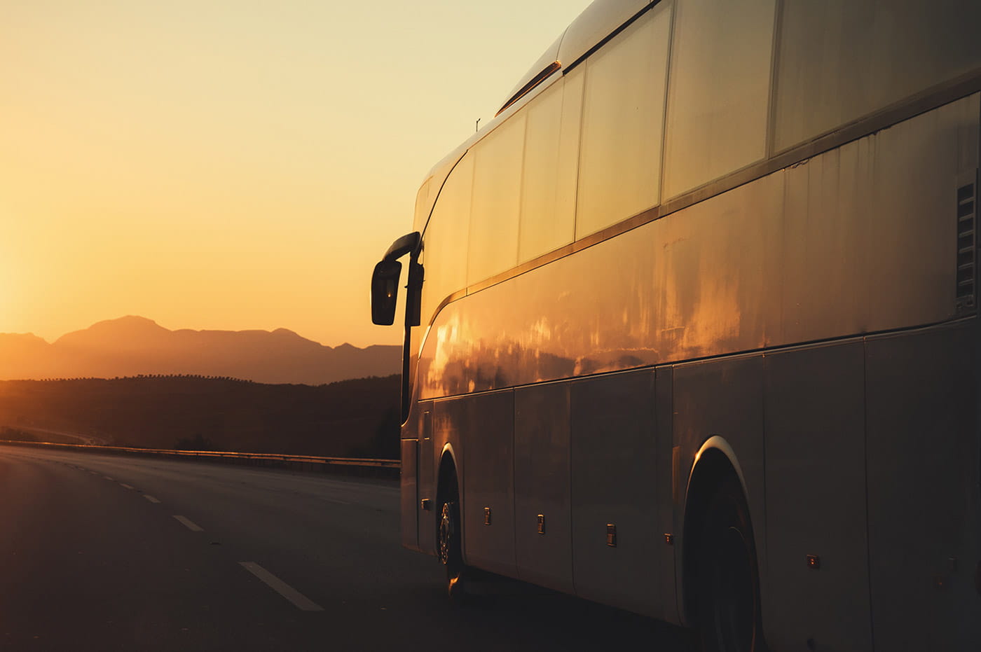 Greyhound bus driving down highway with sunset in background.