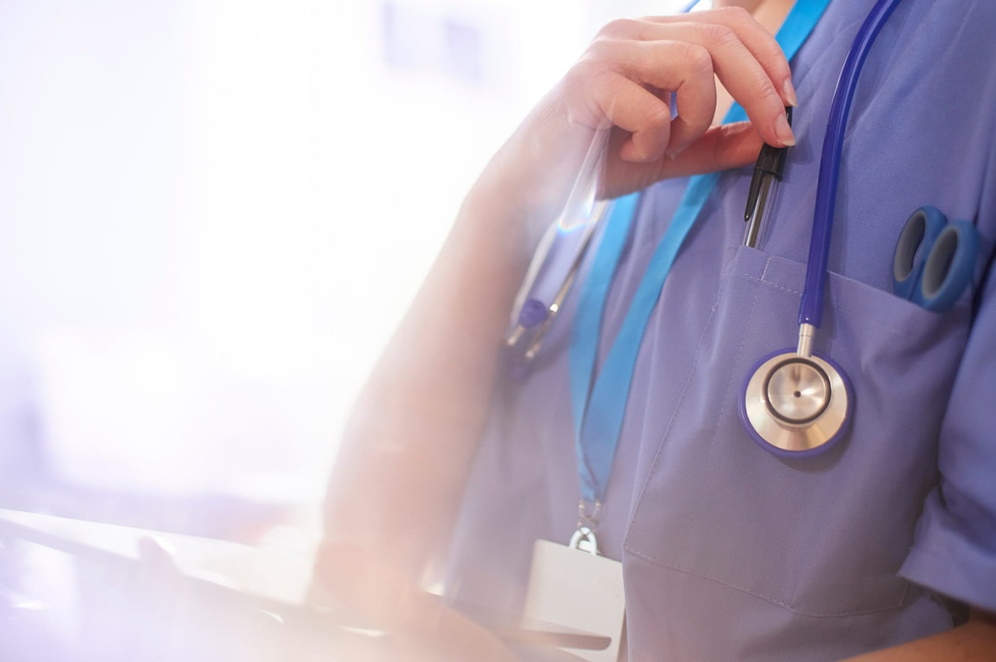 A person wearing scrubs with a stethoscope around their neck holding an iPad.