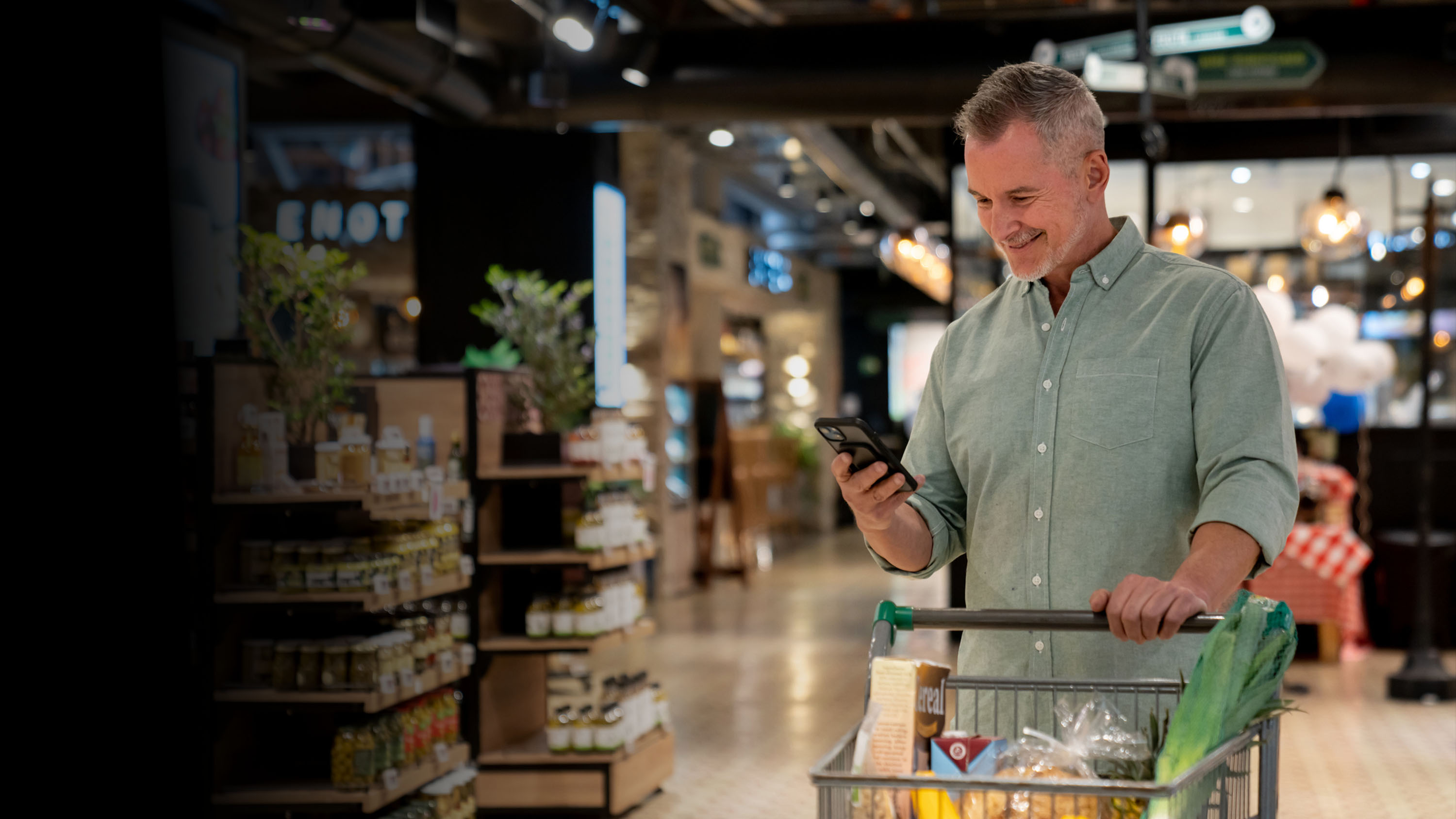 Man pushing a grocery cart and looking at a cellular device in a grocery store