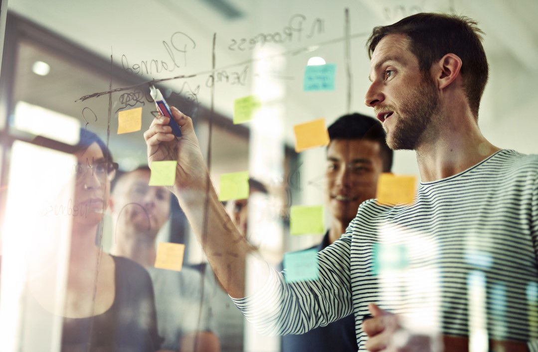 Man writing notes on a clear whiteboard with sticky notes attached to it