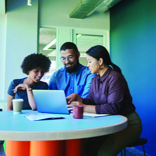 A group of three colleagues gathered around a laptop.