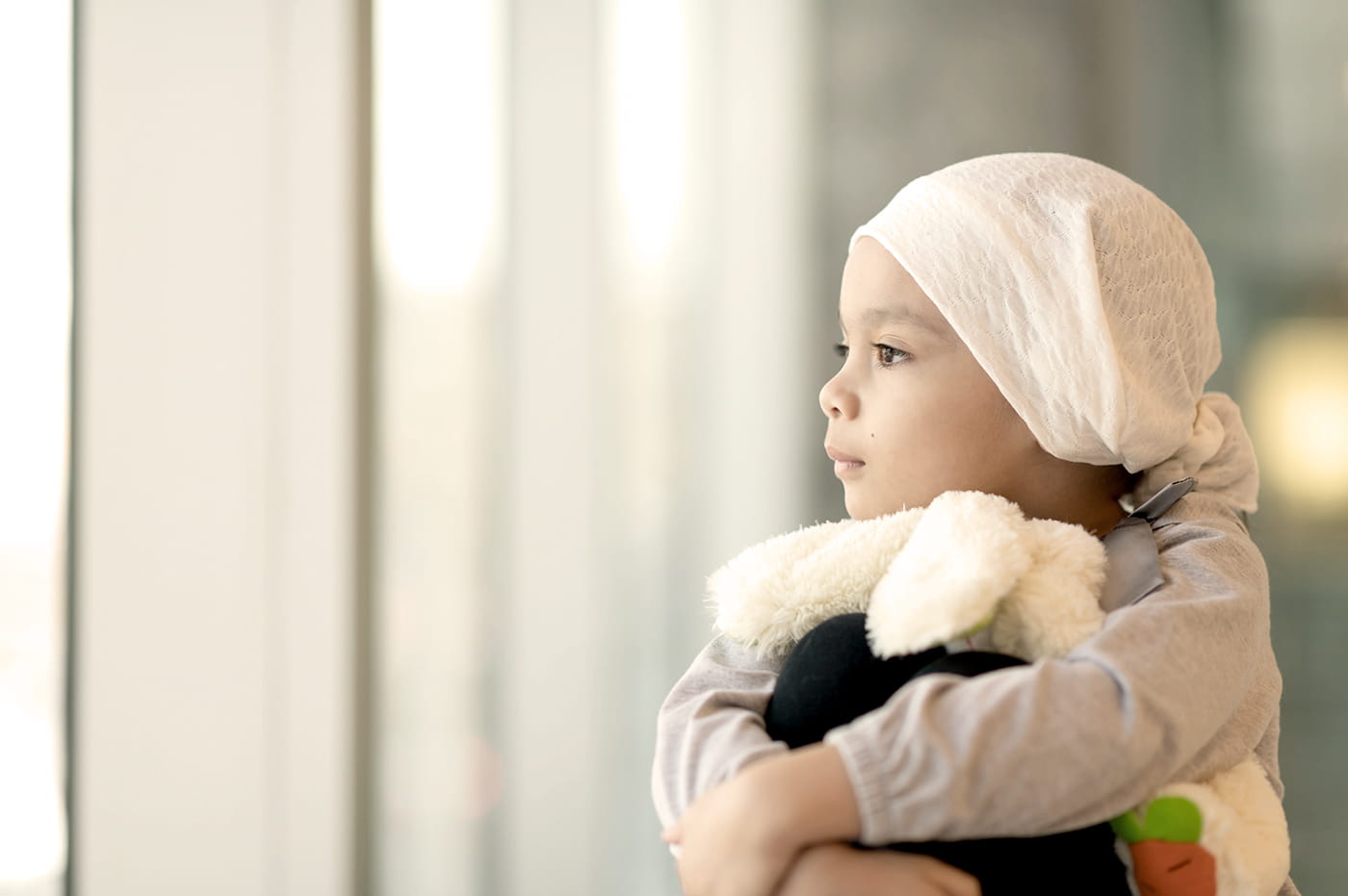 A little girl with a wrap around her head holdng a stuffed animal.