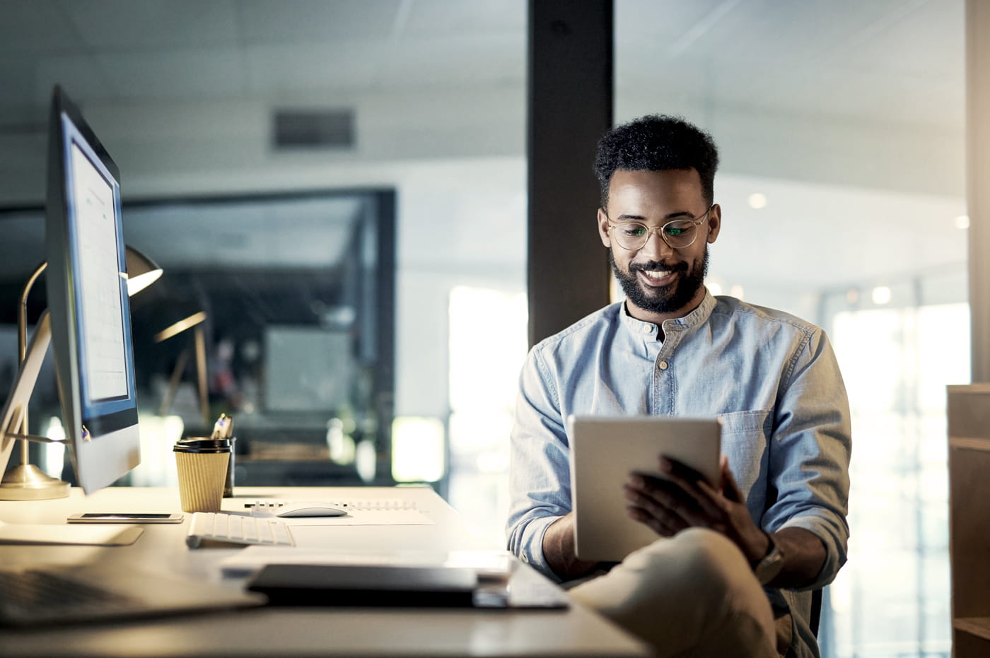 Man sitting at a desk smiling and working on a tablet.